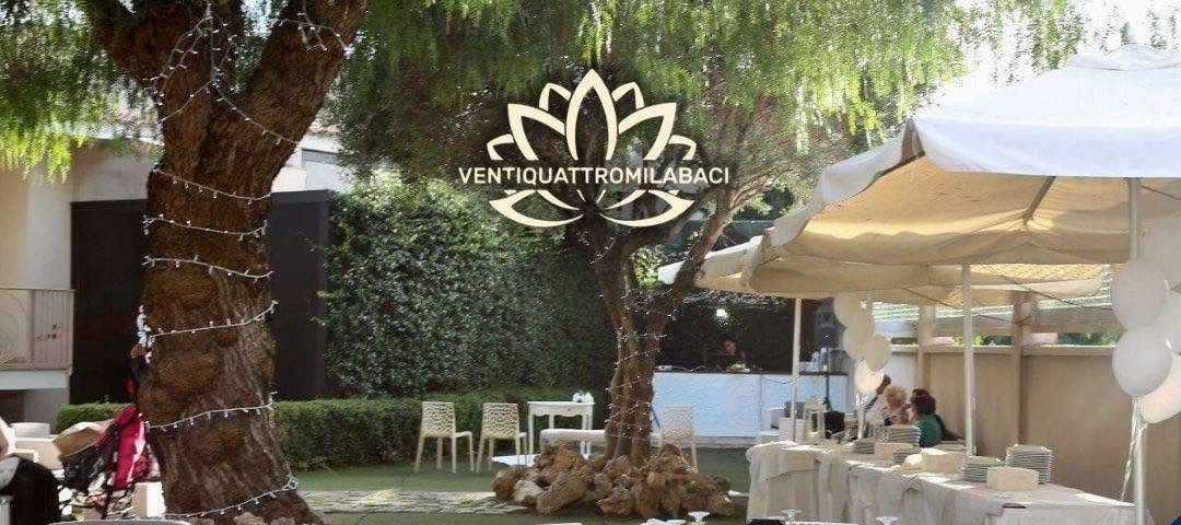 Giardino con grandi ulivi avvolti da luci, tavoli rotondi con tovaglie bianche e gazebo
