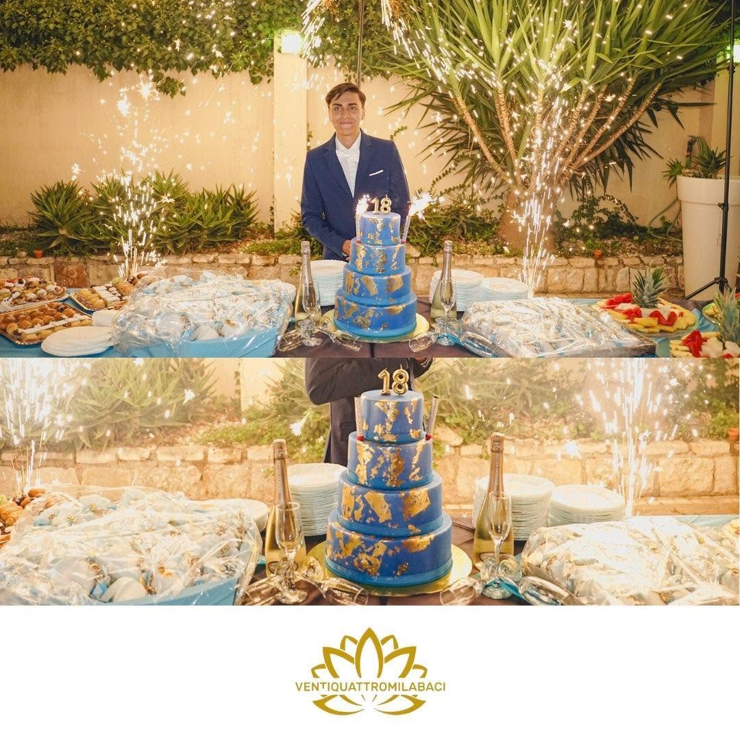 Torta blu a quattro piani con foglia oro e candeline 18 tra fuochi freddi in giardino